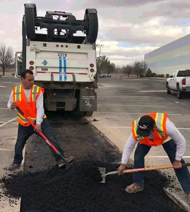 men in construction outfits filling a hole with asphalt img